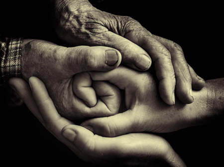 Image of a pair of older hands clasping a pair of younger hands.