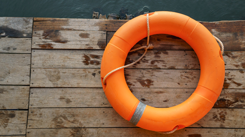Image of an orange life preserver on a dock overlooking water.