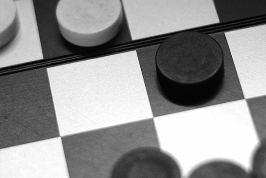 Image of a checkerboard with opposing black and white game pieces.