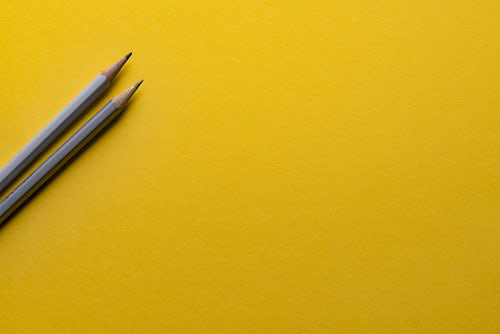 Two gray pencils over a yellow background.