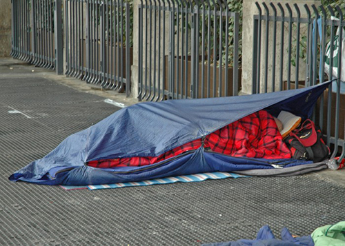 A homeless person in a sleeping bag on a city street.