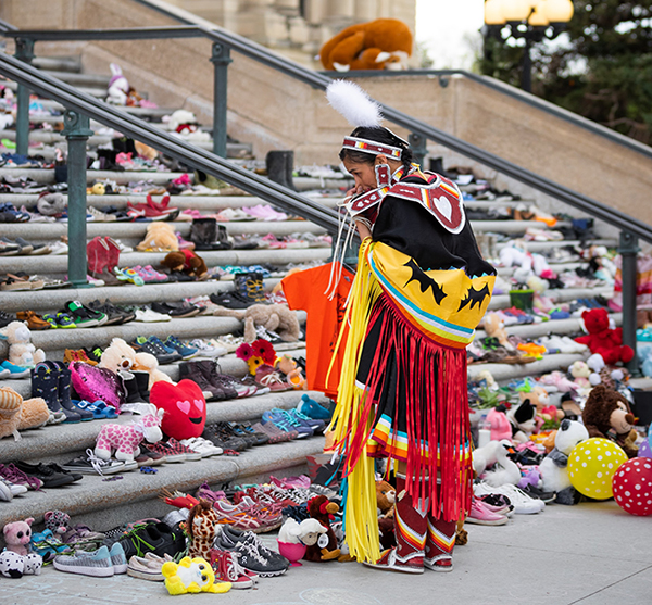 Native American woman in traditional dress, looking at hundreds of stuffed animals on the steps.