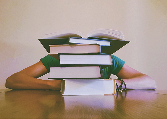 Photo of a stack of books with a person's elbows sticking out from behind them.