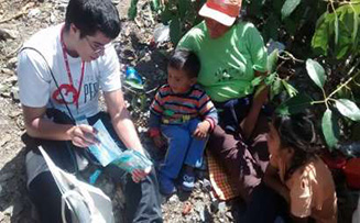 Photo of Ricardo Lewis, Nutre Perú volunteer, reading the story of “El Escuadron Clorito” to a family during a home visit at the family's orchard.