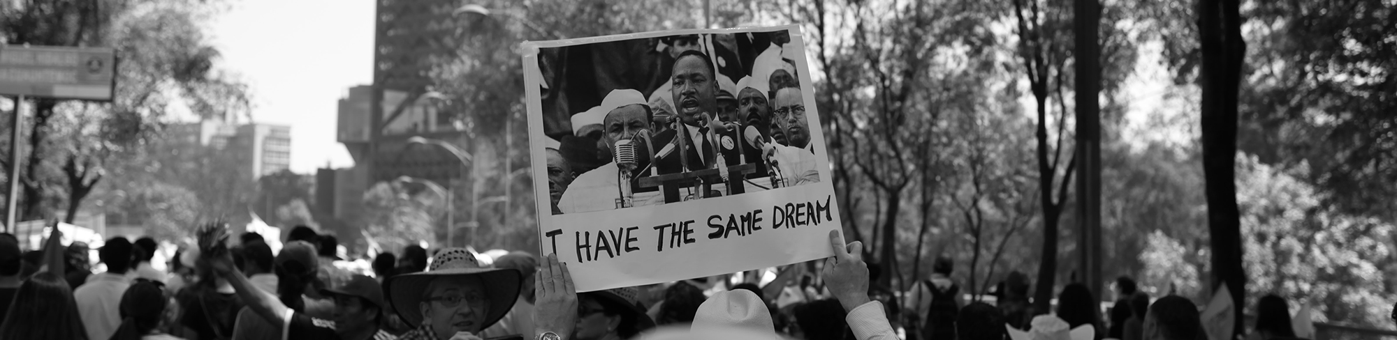 Image of protestors in a crowded street holding a sign with a photo of Martin Luther King, Jr., saying, "I have the same dream."