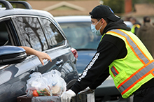 Photo of worker wearing mask distributing food through a car window.