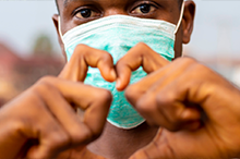 Image of man wearing surgical mask making the sign of a heart with his hands.