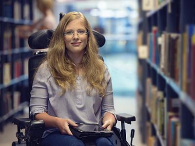 Portrait of young woman in wheelchair in library.