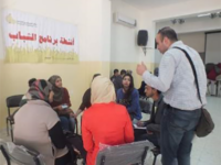 Photo of a Palestinian man standing with a group of women seated around a table.