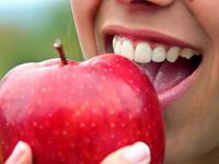 Photo of Latino girl smiling and biting into an apple.